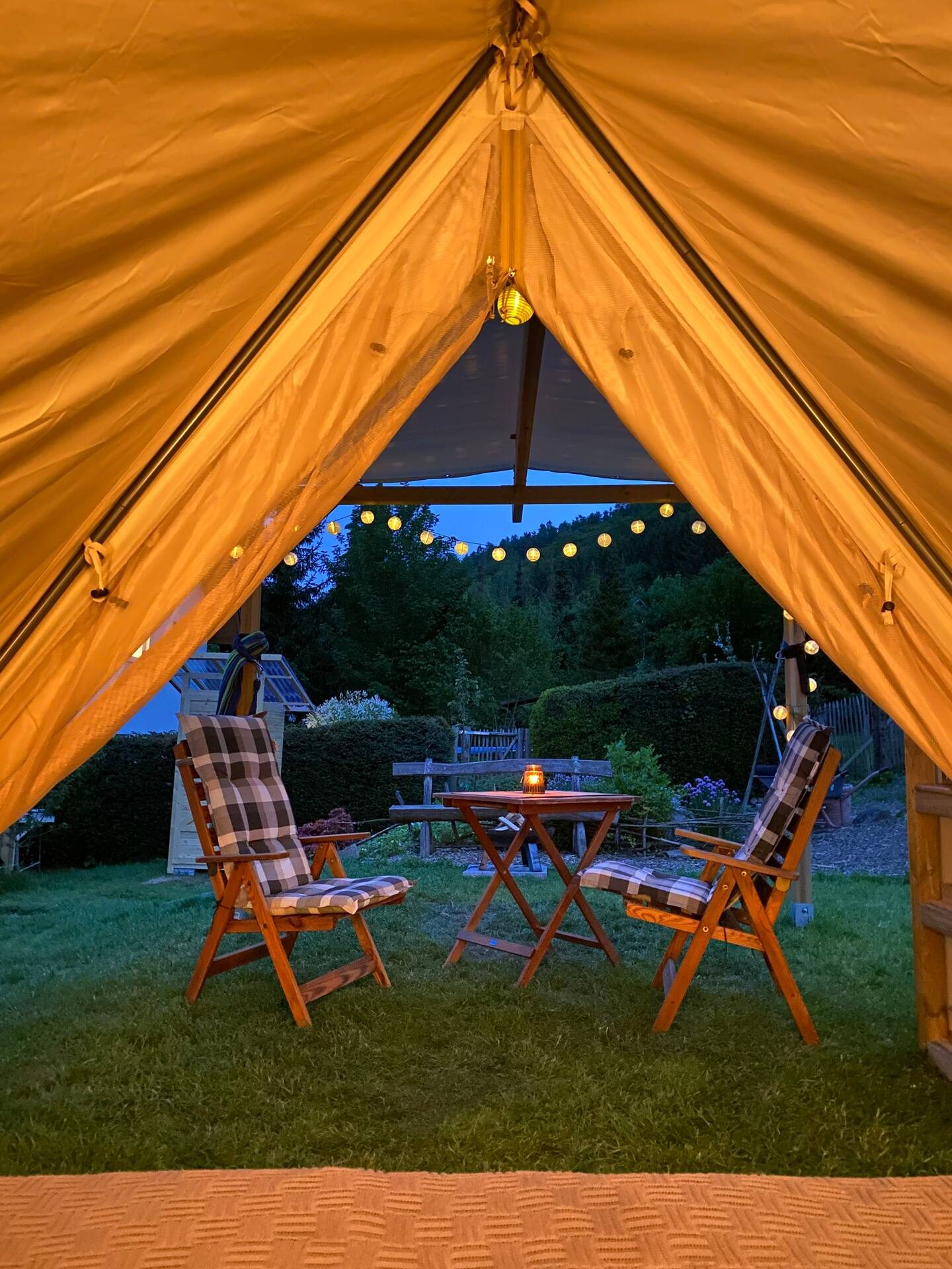 Beleuchtetes Glamping-Zelt am Abend mit Blick in den Garten